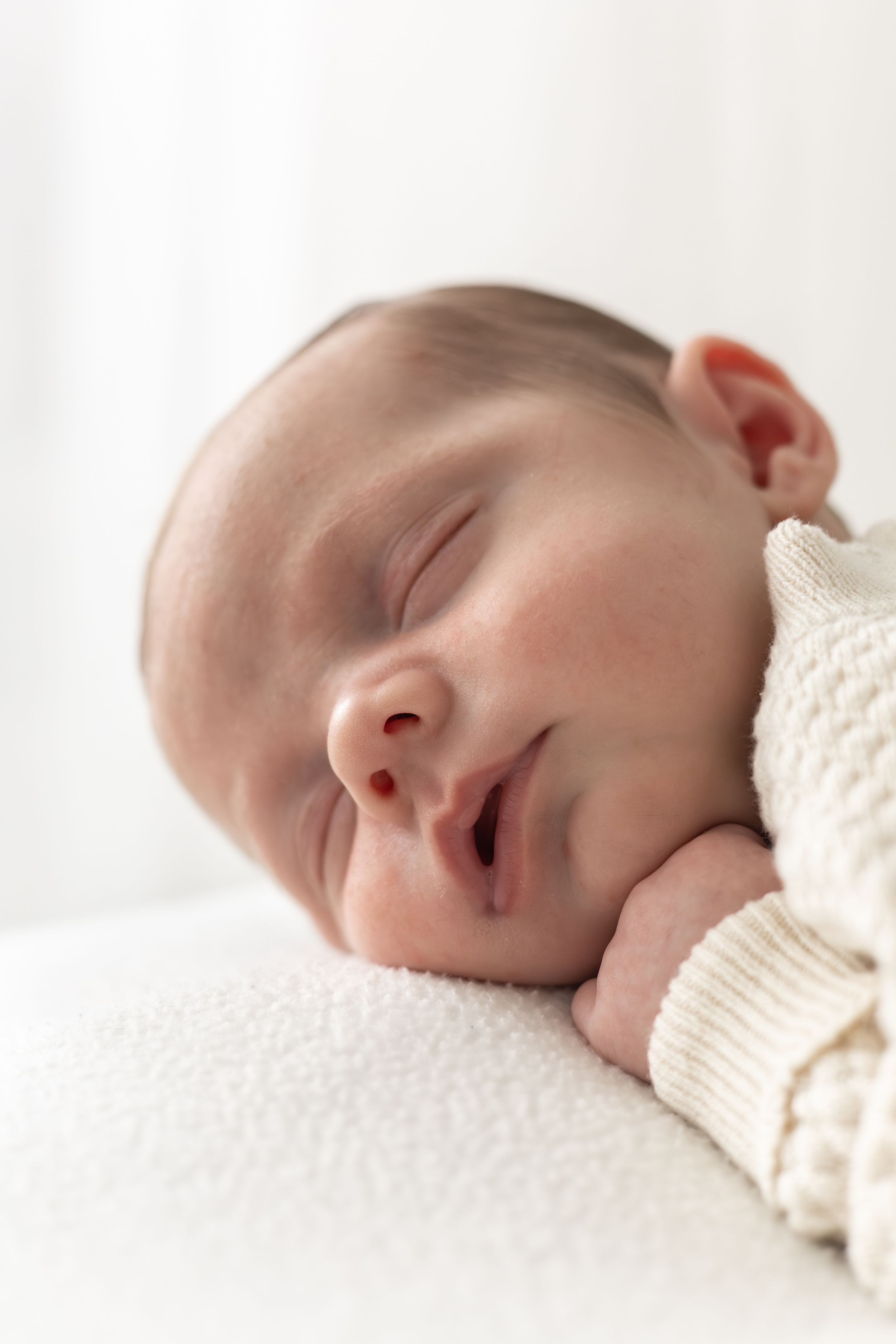 Peaceful newborn baby sleeping soundly, wearing a cream knit outfit, resting on a soft white blanket.