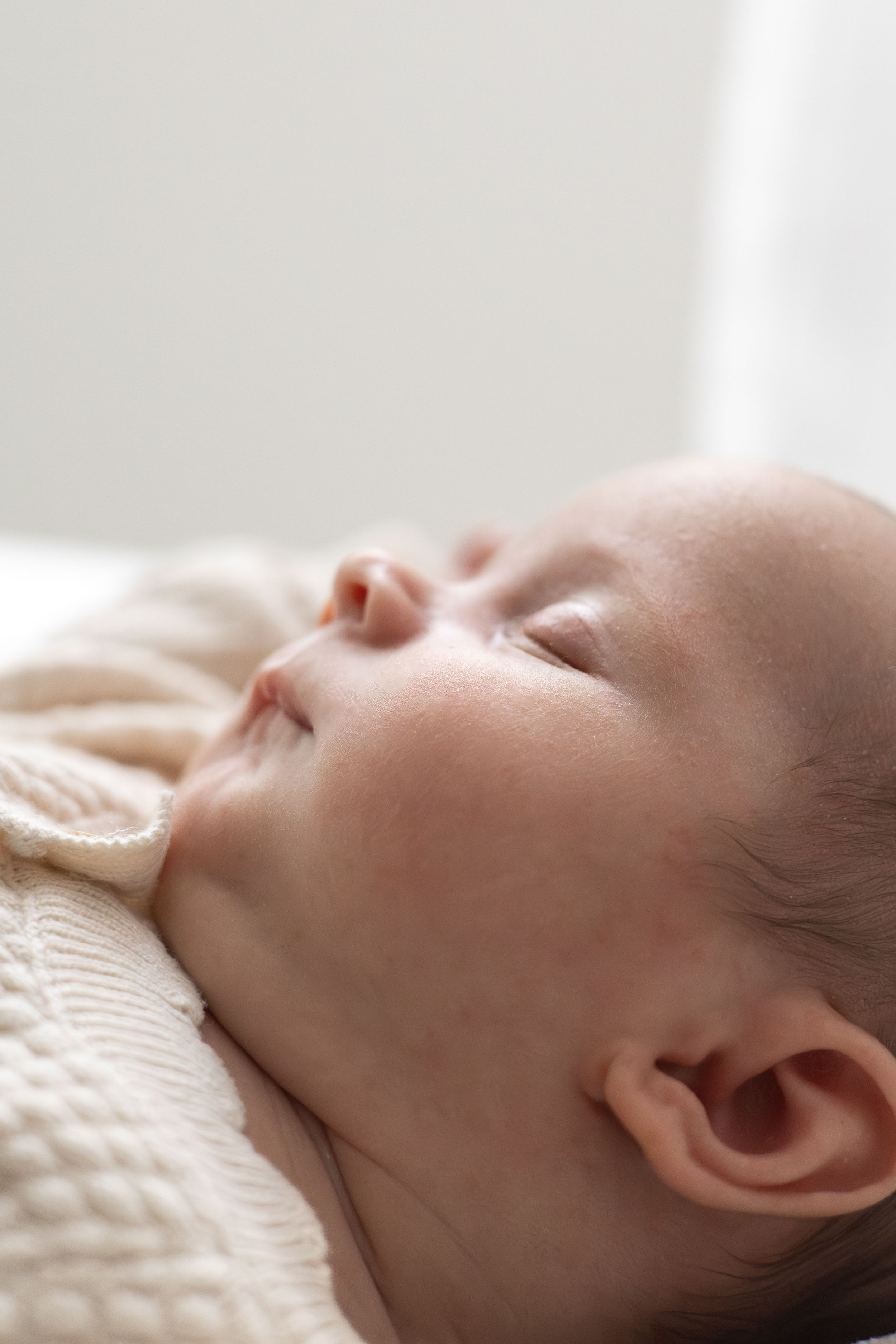 Peaceful newborn baby sleeping soundly, wrapped in a soft cream knit blanket, close-up portrait with soft natural light.