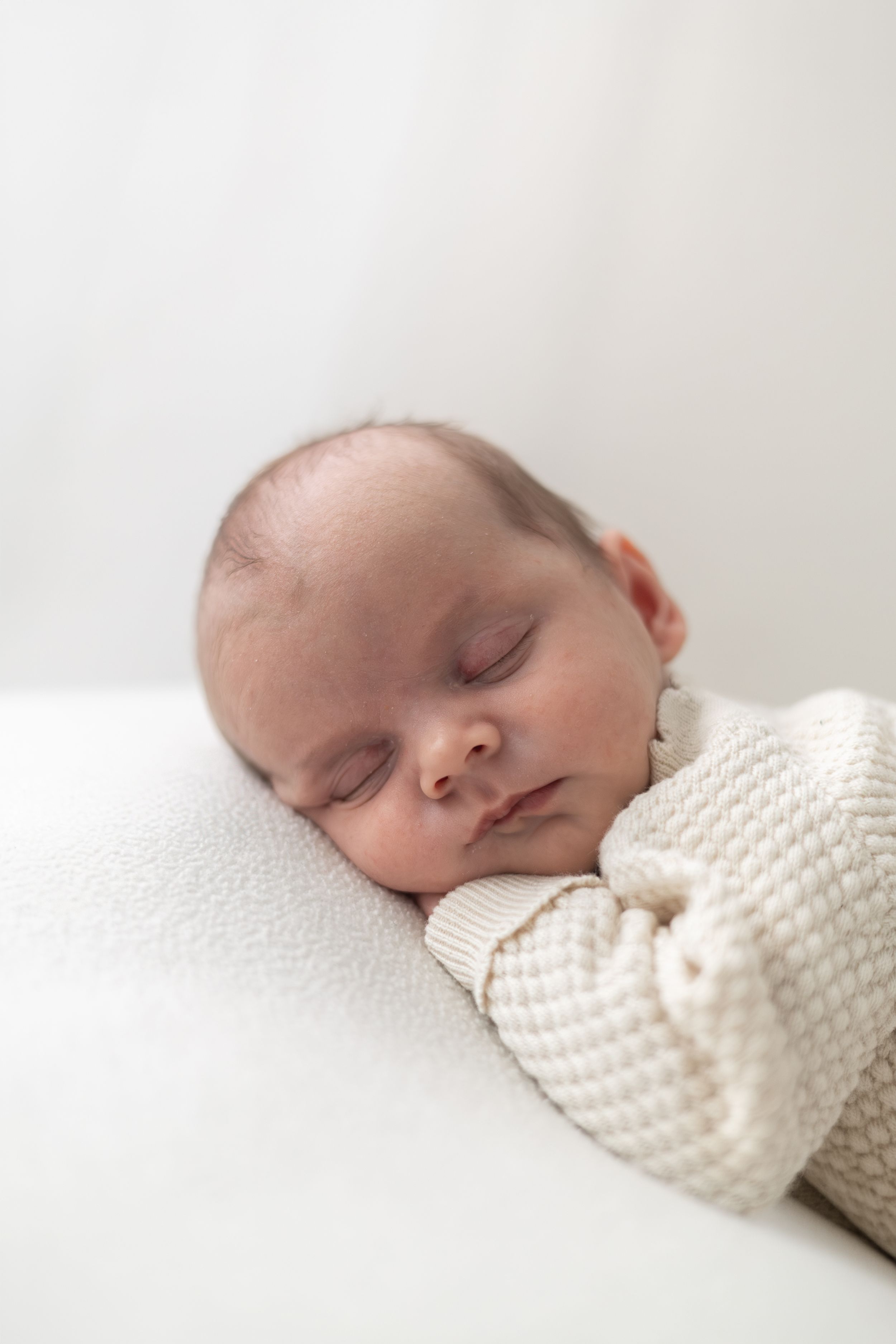 Peaceful newborn baby sleeping in cream knit outfit on white blanket