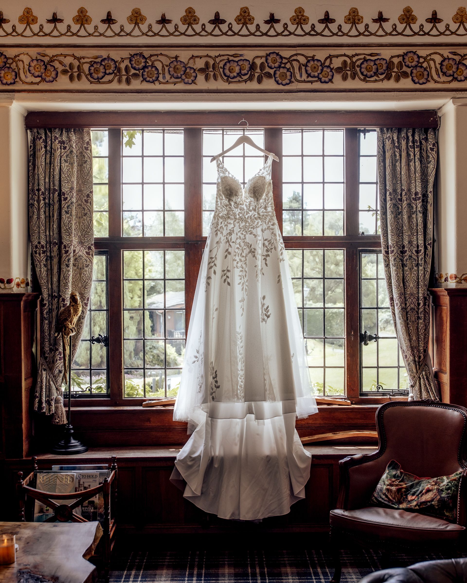 Elegant lace wedding dress hanging in front of a traditional window at Broadoaks Country House