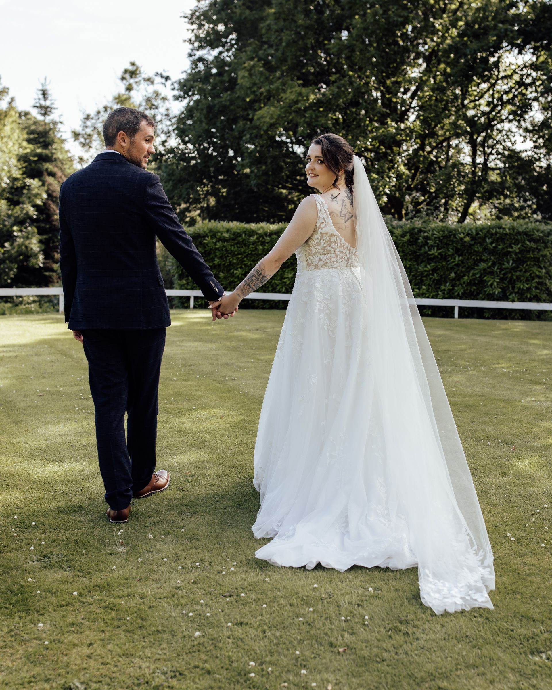 Bride looking back at the camera while walking hand in hand with her groom in the gardens