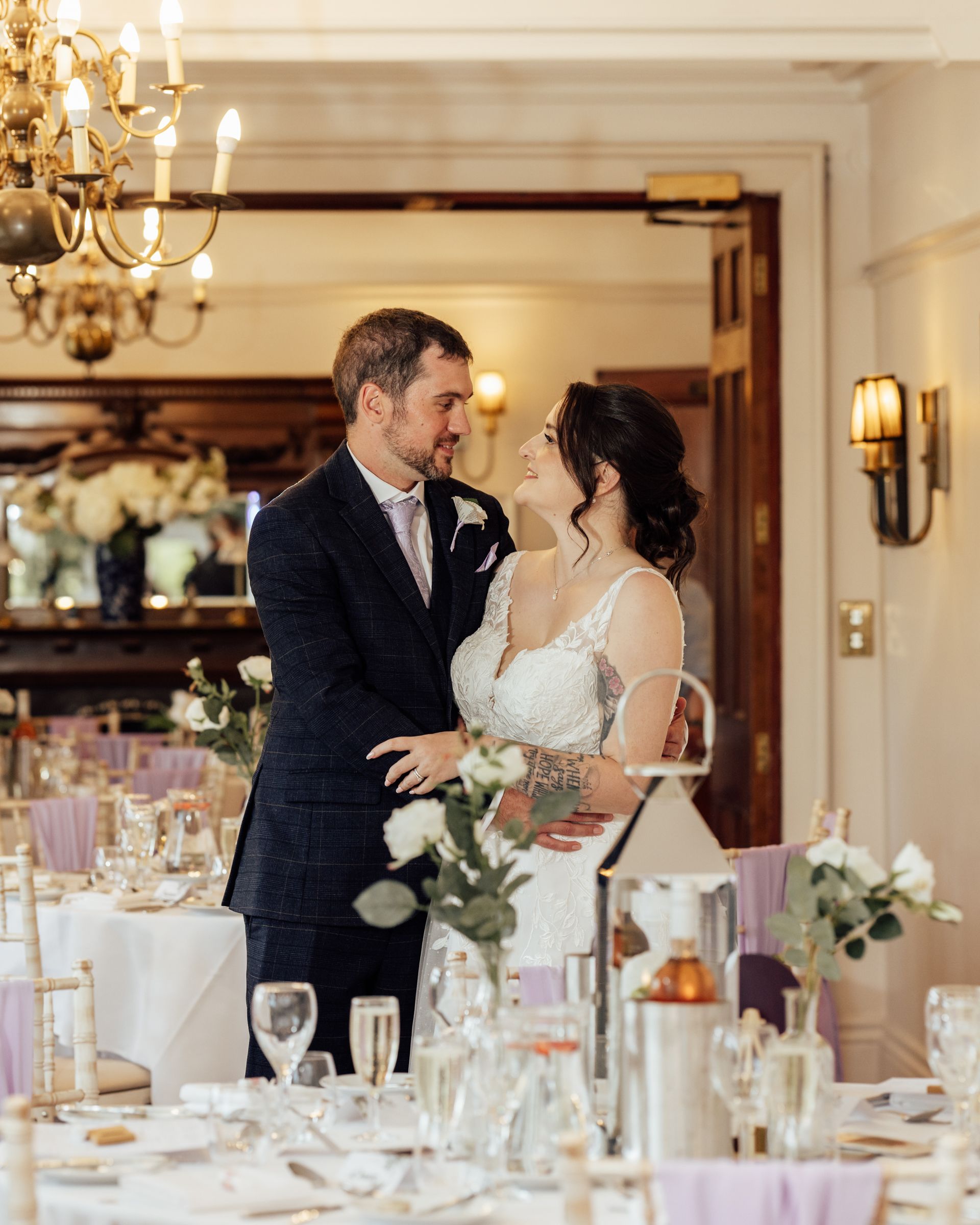 Bride and groom share a romantic moment in an elegantly decorated wedding reception hall with candlelit tables.