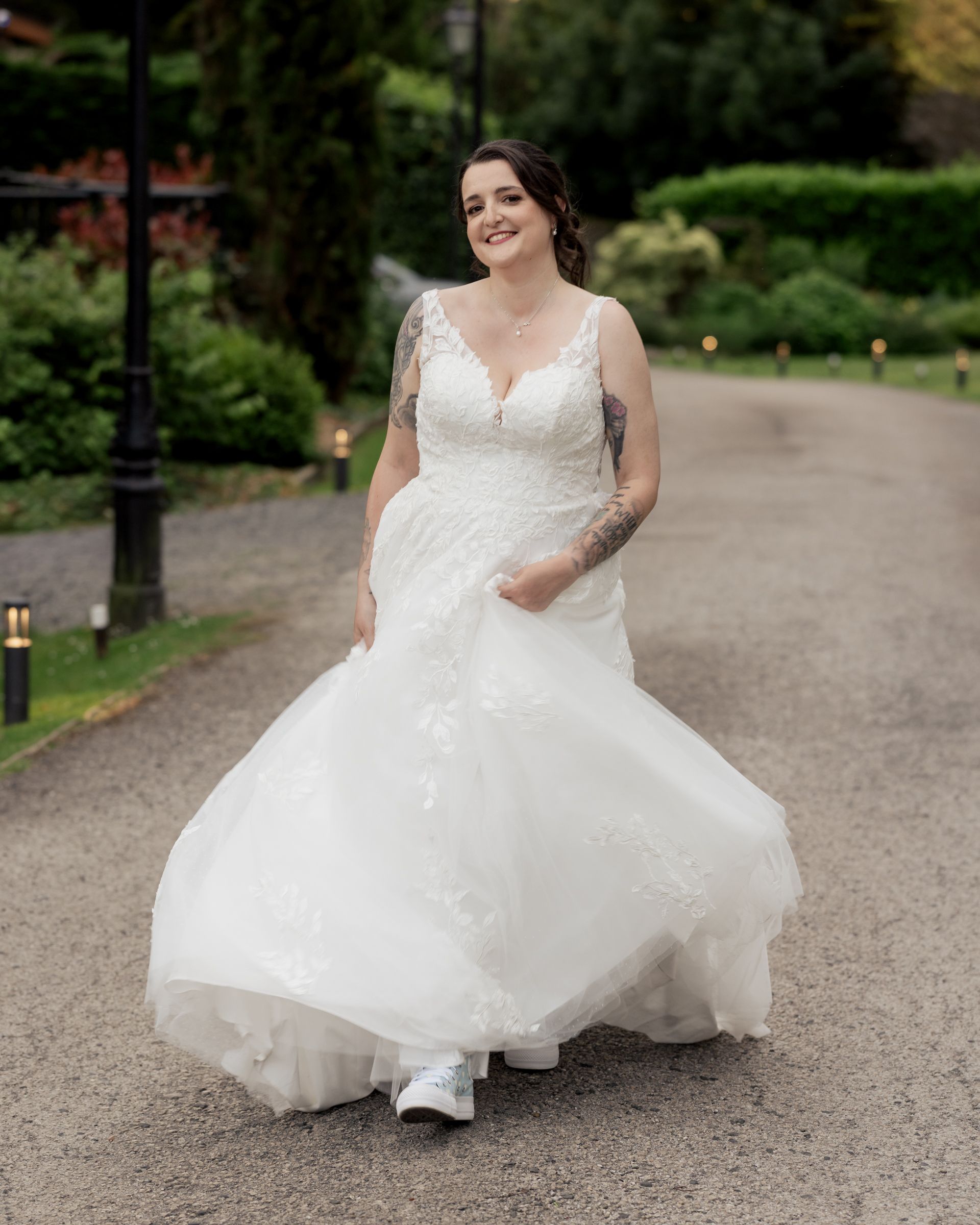 Bride smiling in her lace wedding dress and trainers during relaxed bridal portraits at Broadoaks