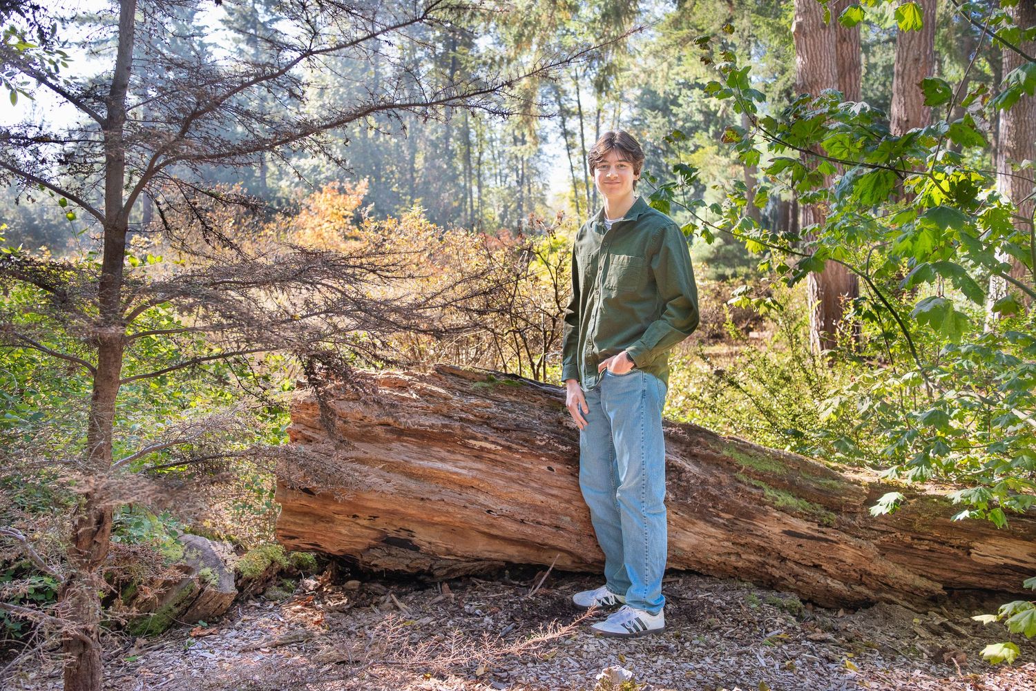 High school senior standing beside a fallen log in the woods at Lake Wilderness Park