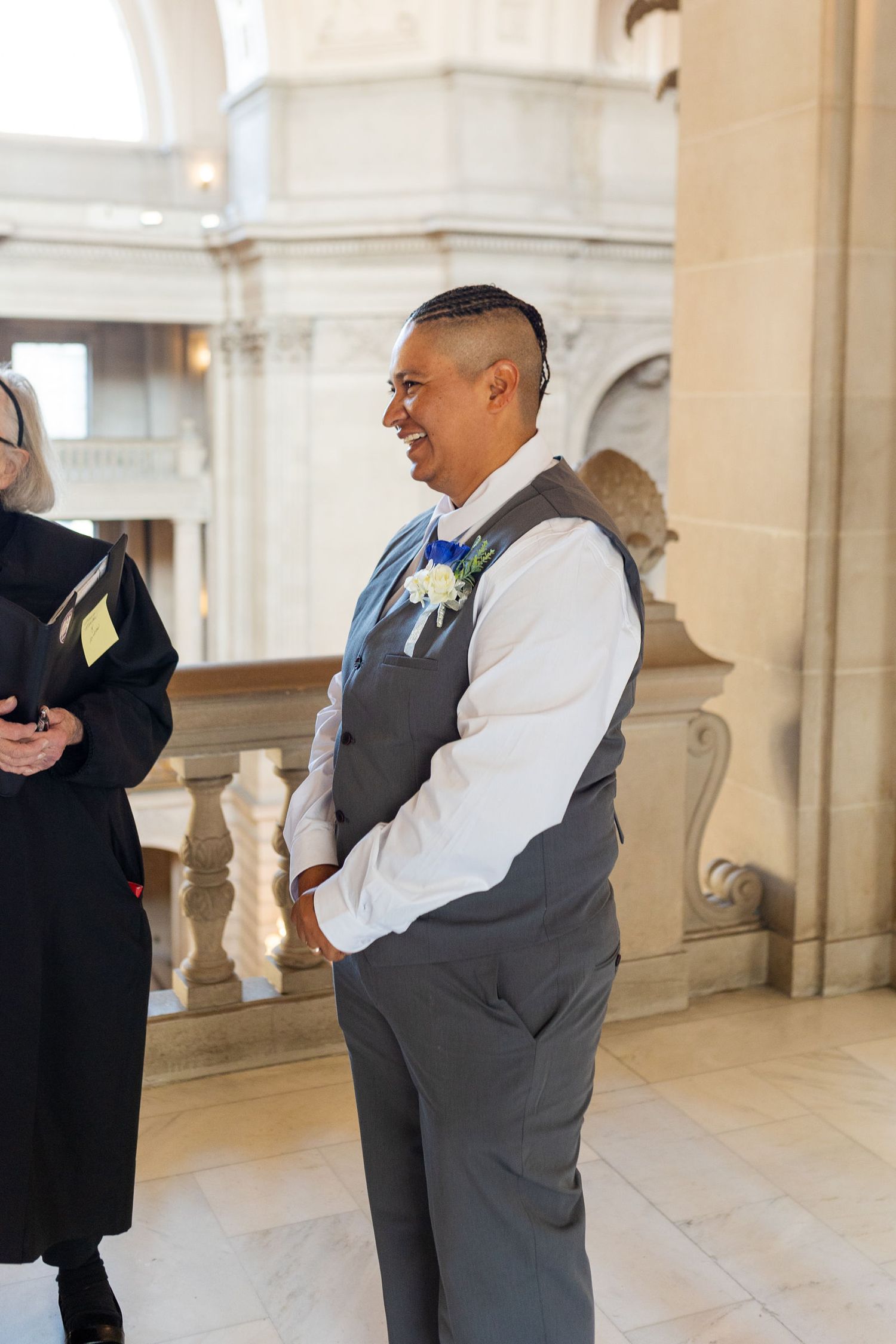 Smiling groom in gray vest with boutonniere at a San Francisco City Hall wedding ceremony.