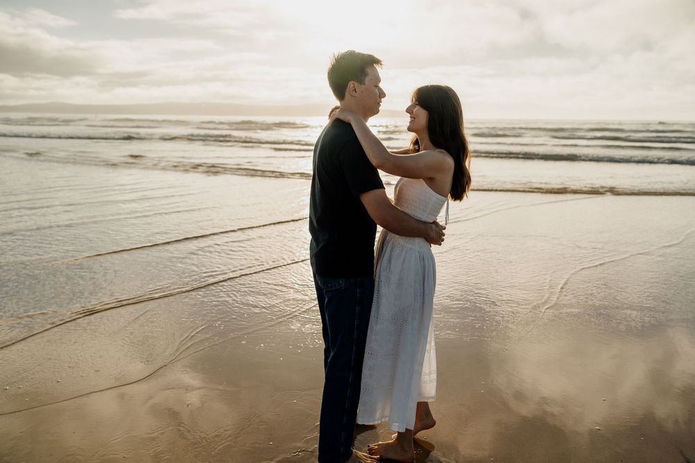 Couple embracing romantically on a beach at sunset with golden reflections on wet sand.
