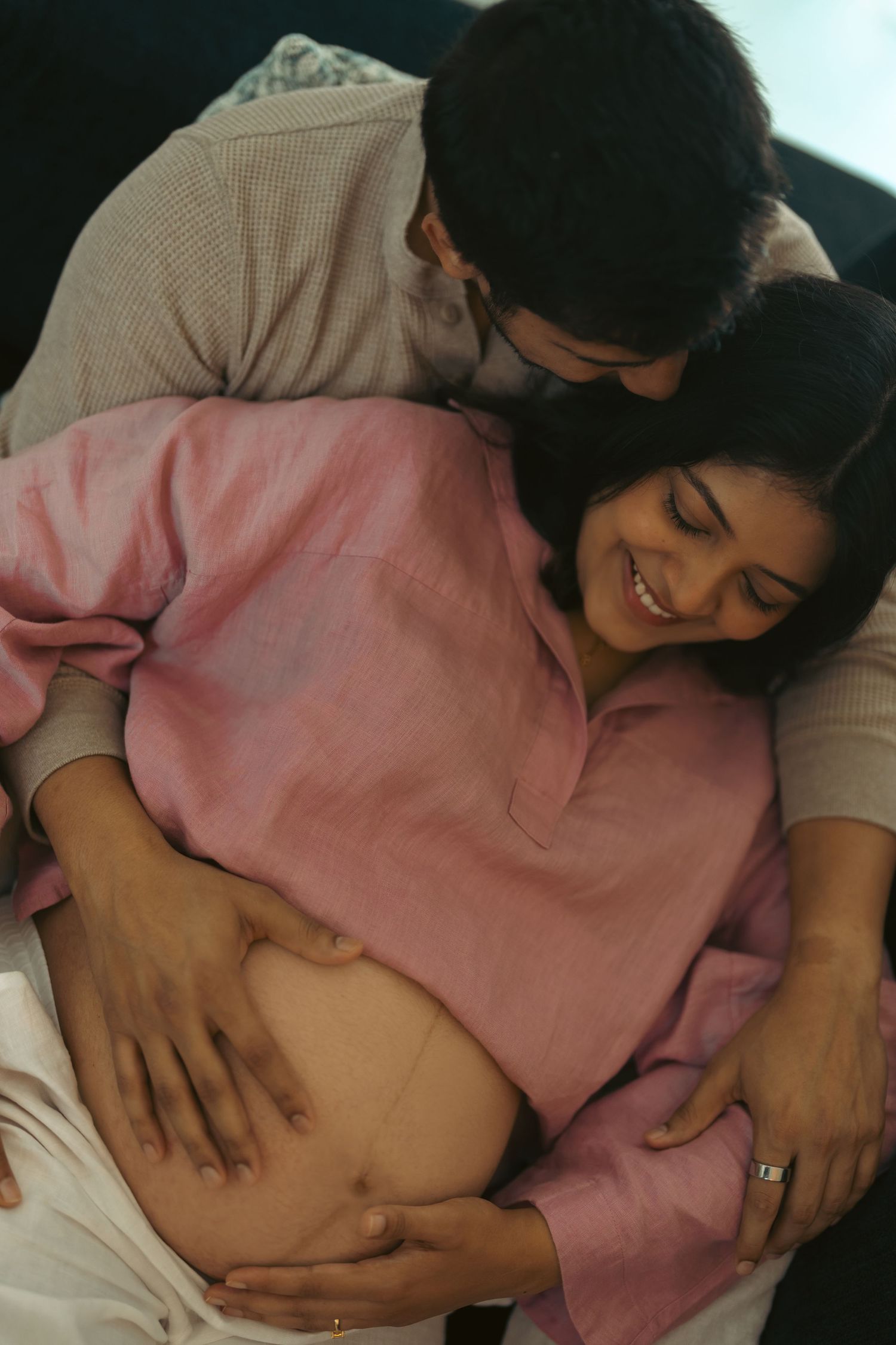 Smiling expectant mother with her partner holding her baby bump during an in-home maternity shoot in Dubai