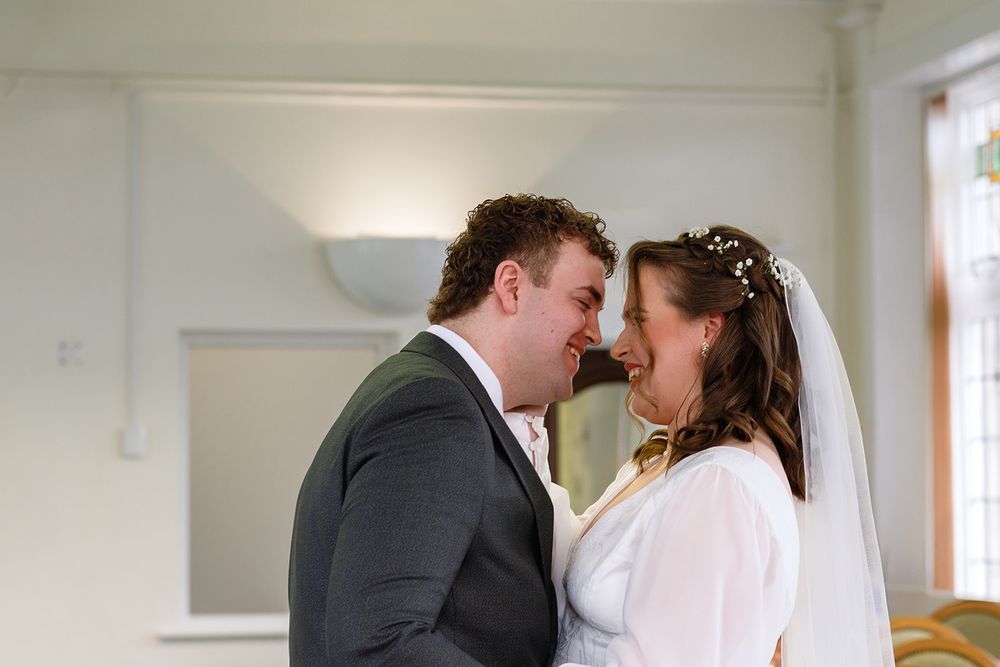 A joyful newlywed couple sharing an intimate moment, bride in white veil and groom in gray suit, smiling face to face.