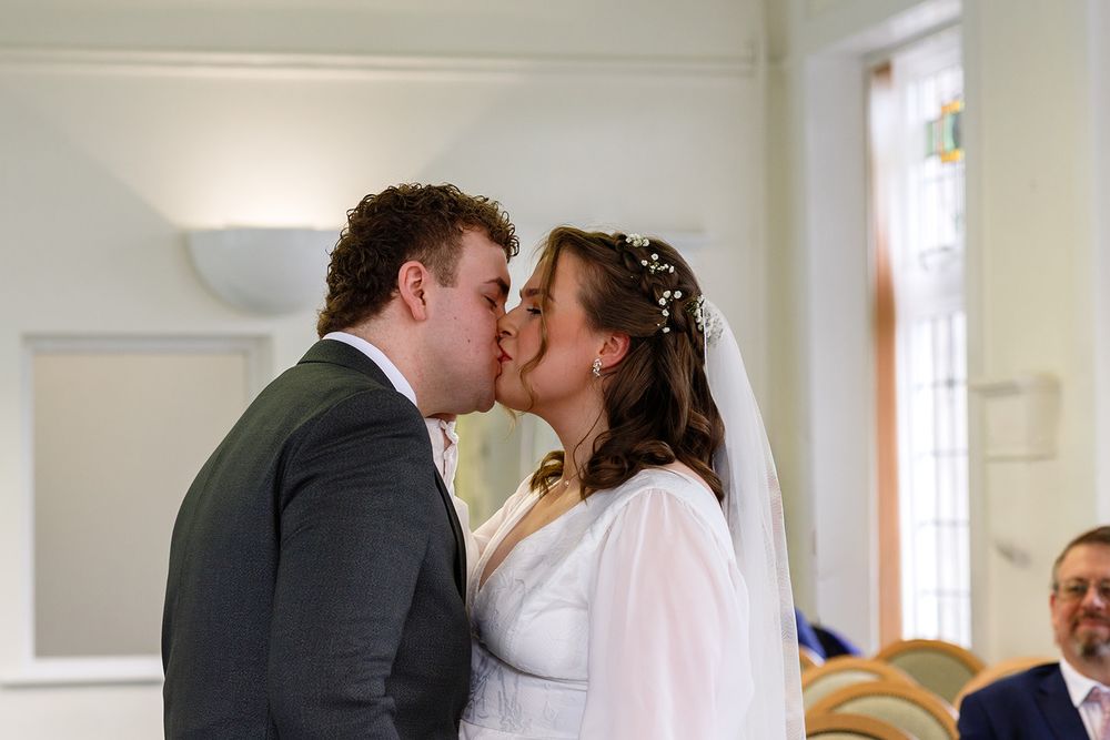 Bride and groom share their first kiss at wedding ceremony indoors.
