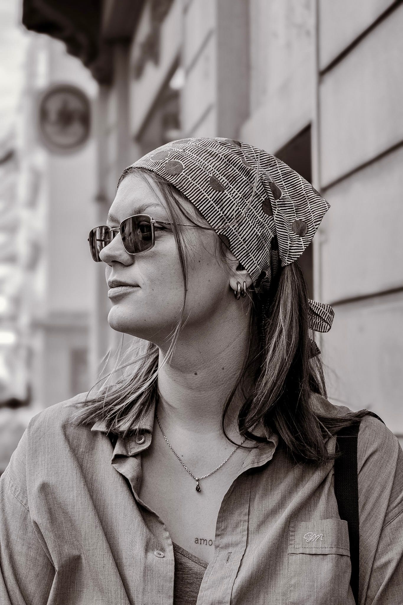 Black and white portrait of stylish woman wearing headscarf and sunglasses on city street.
