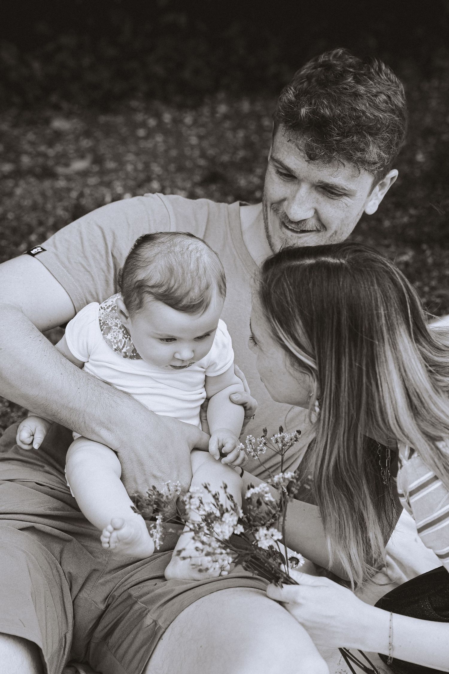 Black and white photo of young family with father holding baby girl outdoors.