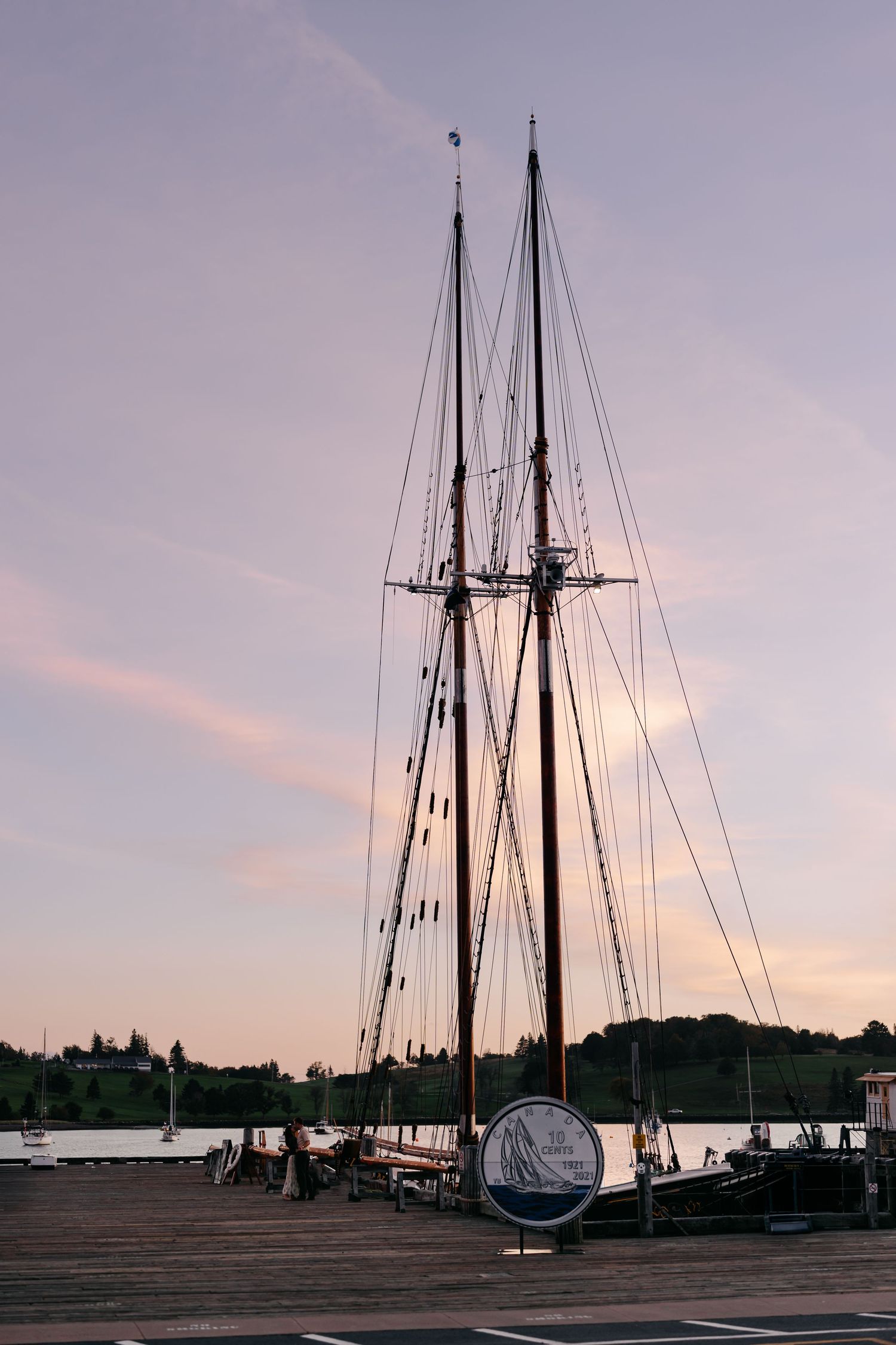 Bluenose Ship masts silhouetted against a pastel sunset sky at a wooden dock marina.