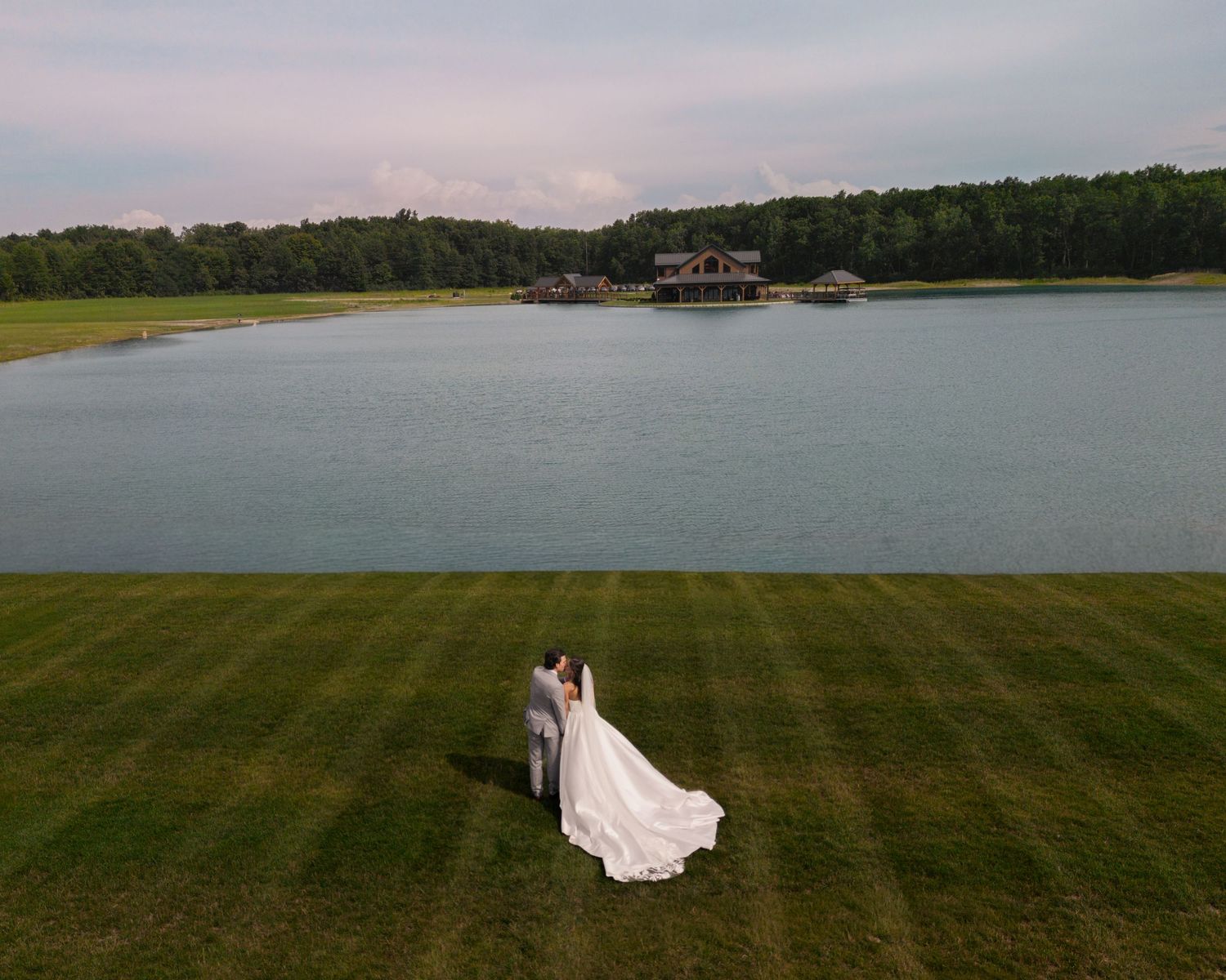 Aerial view of bride and groom embracing on lush green lawn beside a serene lake at the Tall Oaks Resort wedding venue in Sheffield Village