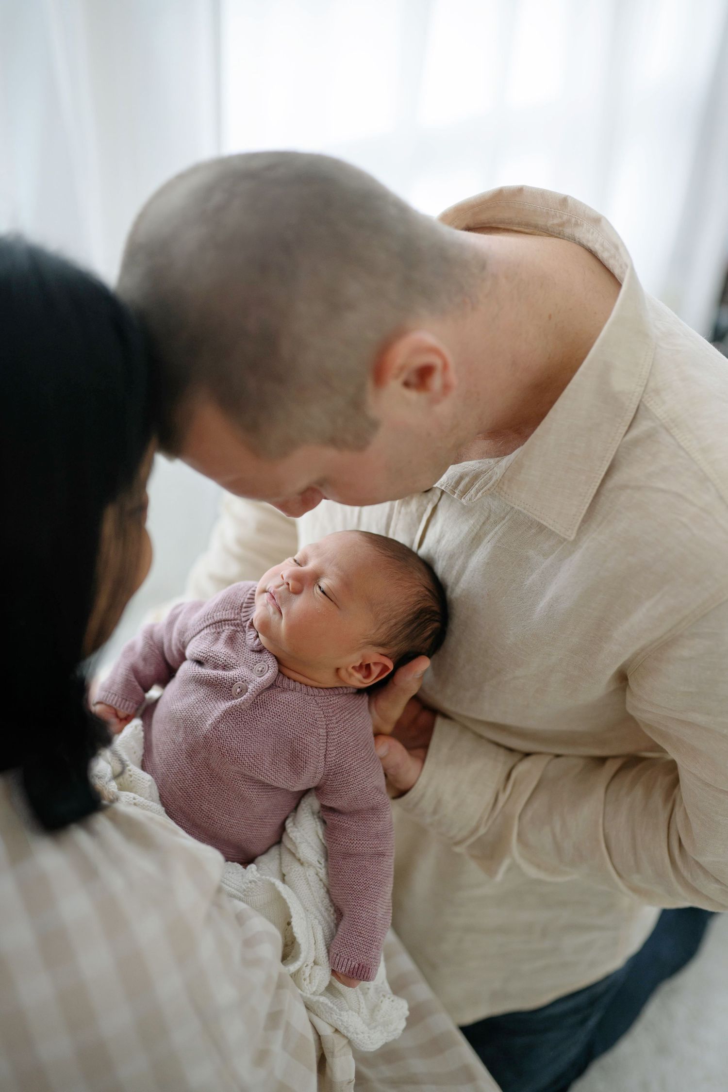 Parents lovingly gazing at their sleeping newborn baby dressed in a pink onesie.
