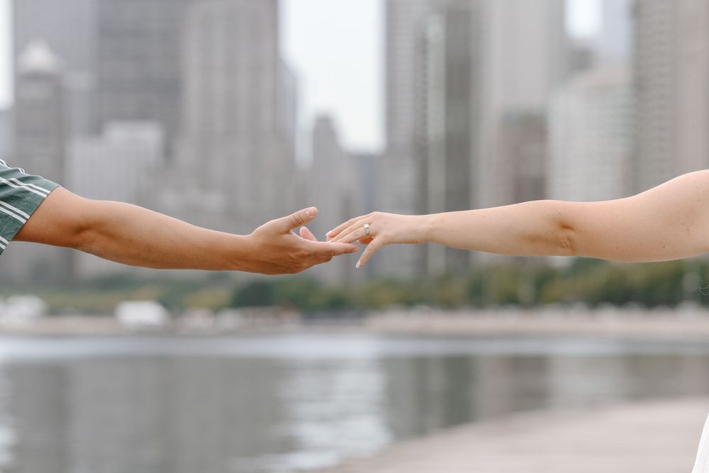 Two hands reaching toward each other with a city skyline and waterfront in the blurred background.