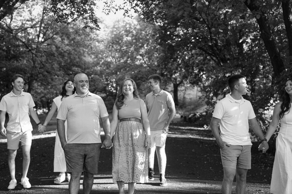 Black and white photo of a smiling family walking together on a tree-lined path outdoors.