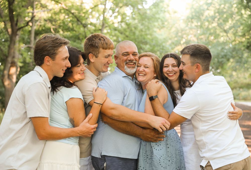 Happy multigenerational family hugging and laughing together outdoors in a sunny green park setting.