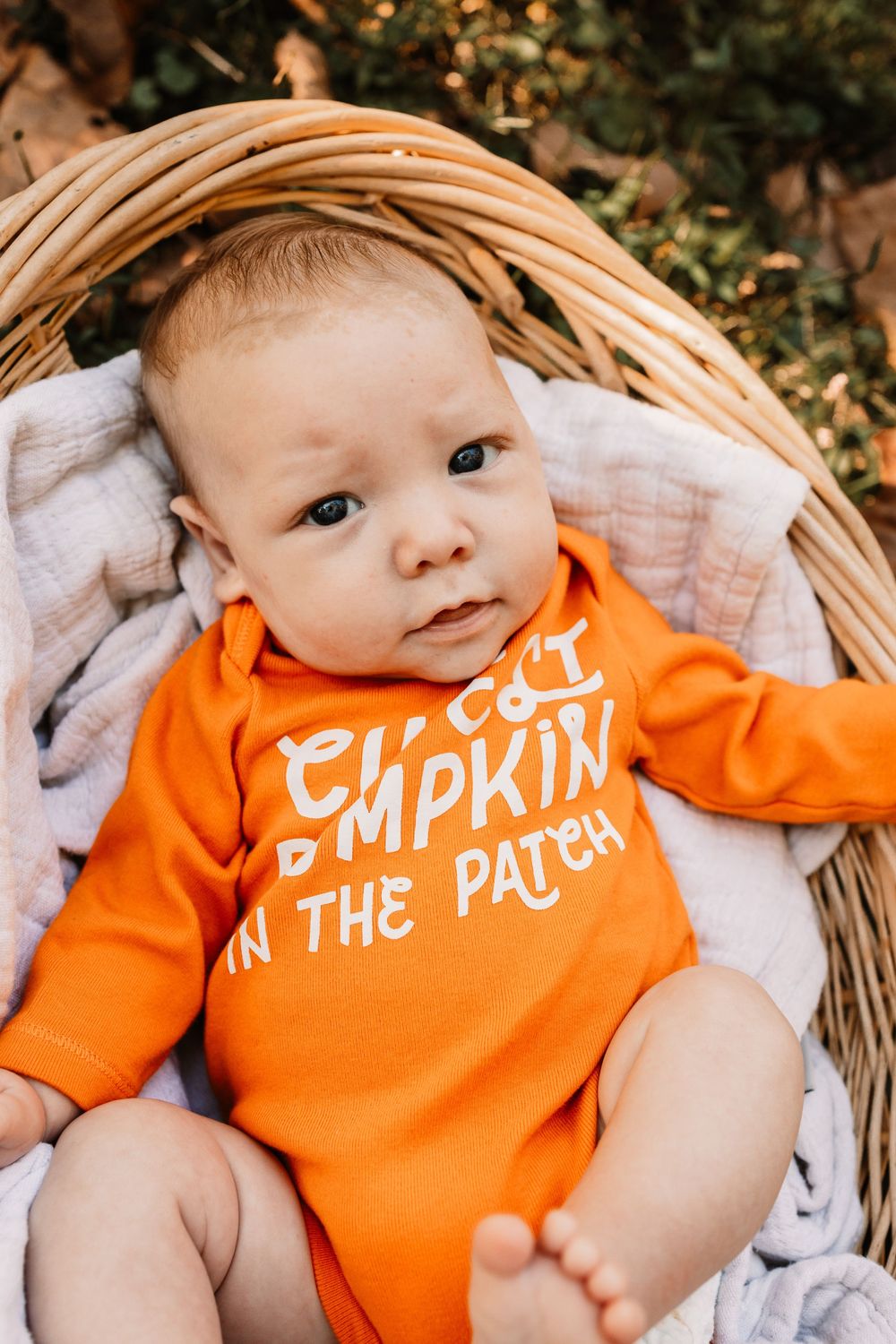 Close-up of a baby in an orange Cutest Pumpkin in the Patch onesie during a lifestyle family photography session in Oak Ridge, Tennessee.