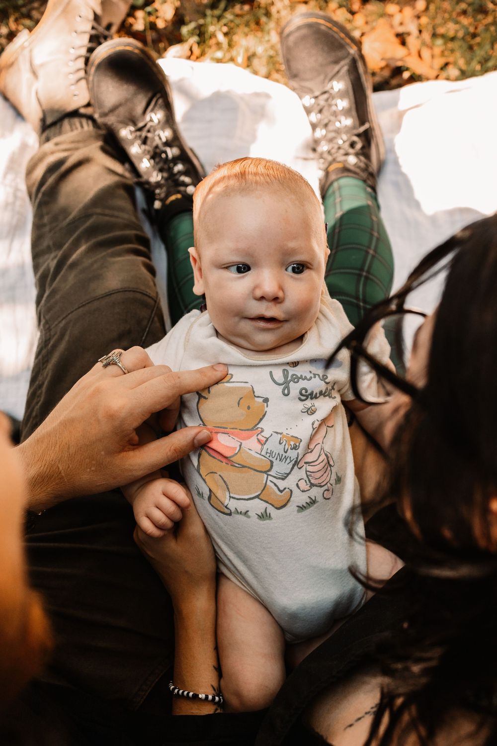 Smiling baby in a Winnie the Pooh onesie lies across an adult's lap during a lifestyle family photography session in Oak Ridge, Tennessee.