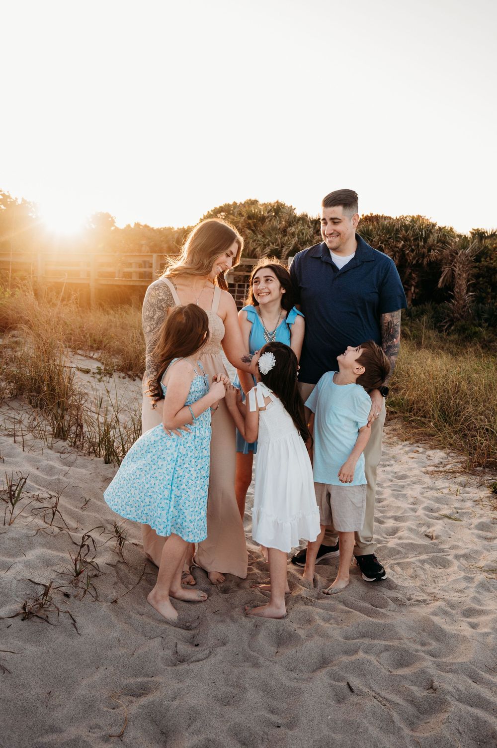 Family of five sharing a joyful moment on a sandy beach at golden sunset hour.