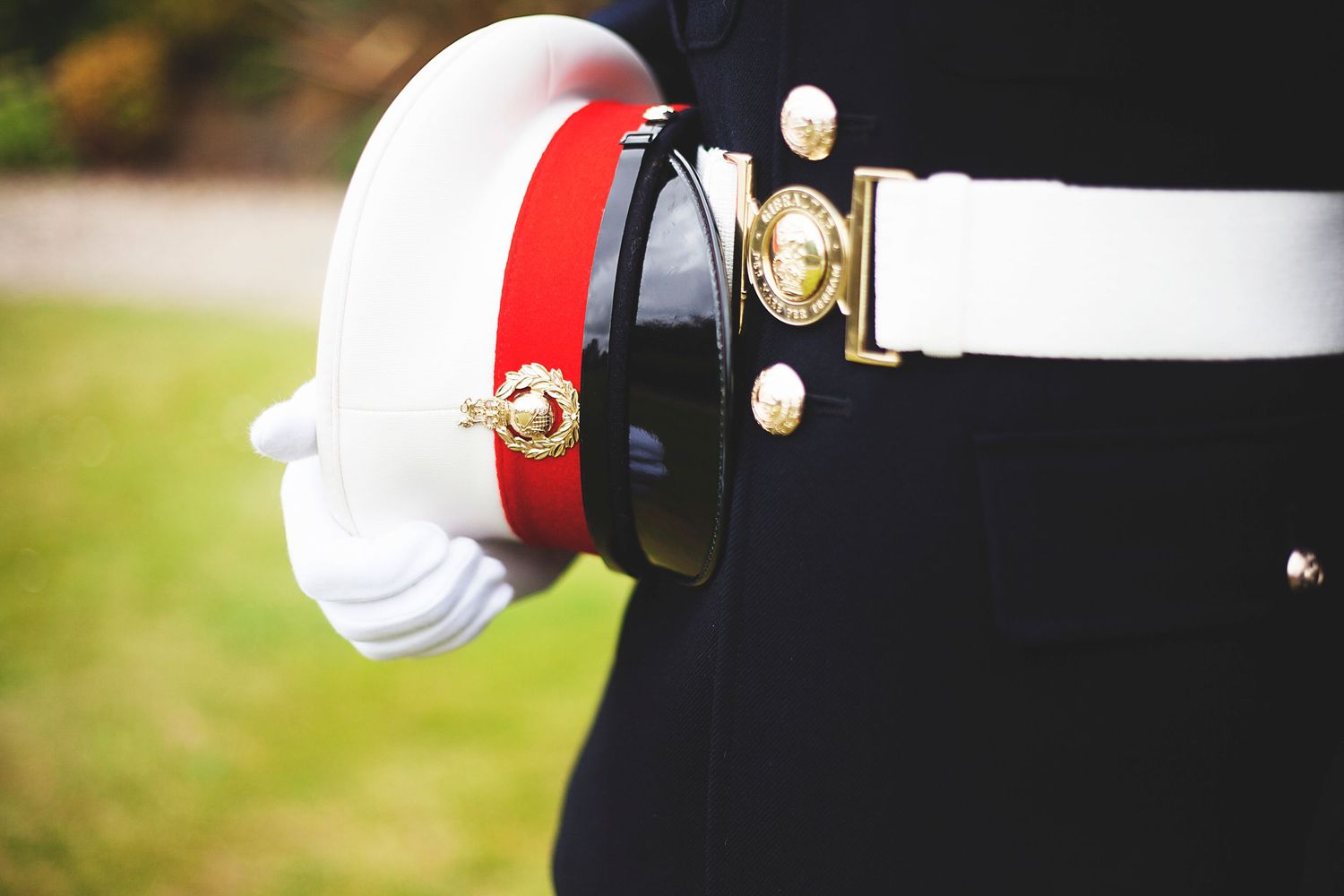 Marine in dress uniform holding a white and red ceremonial cap with gold buttons and white gloves.