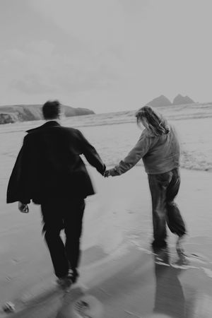 Black and white photo of a couple holding hands running on a beach, captured with motion blur effect.