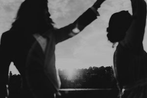 Black and white silhouette of two women dancing outdoors with sunlight glowing between them.