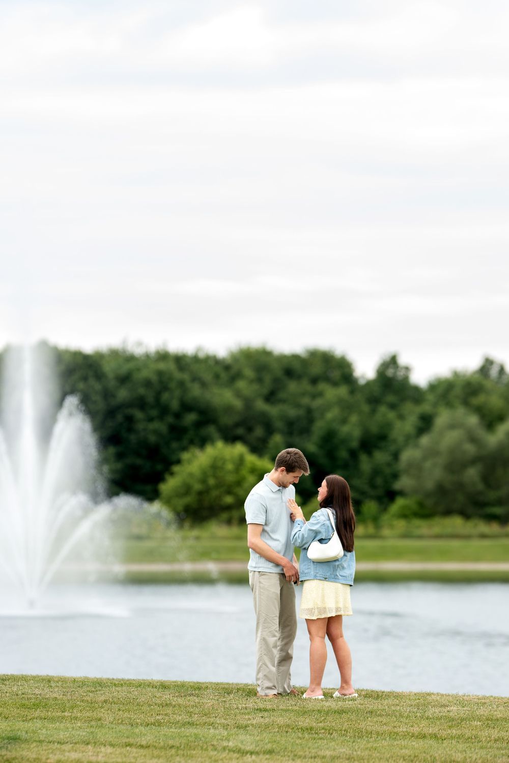 Happy couple holding hands and facing each other by a tranquil pond with fountains in a park.