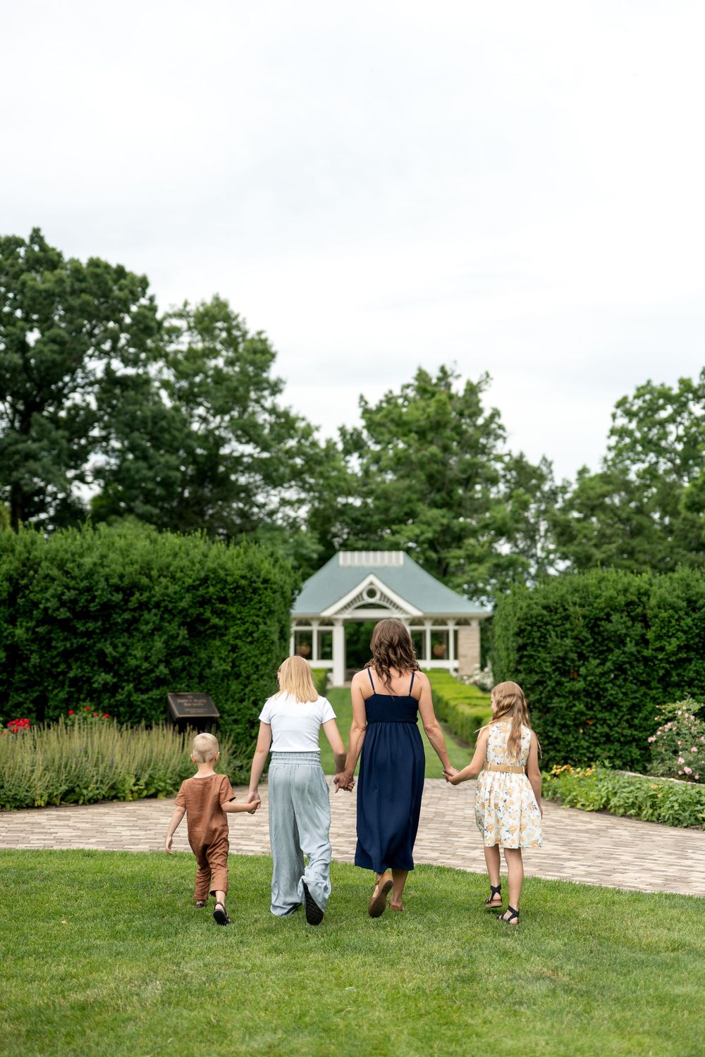 A mother holds hands with three children walking toward a cottage in a green garden.