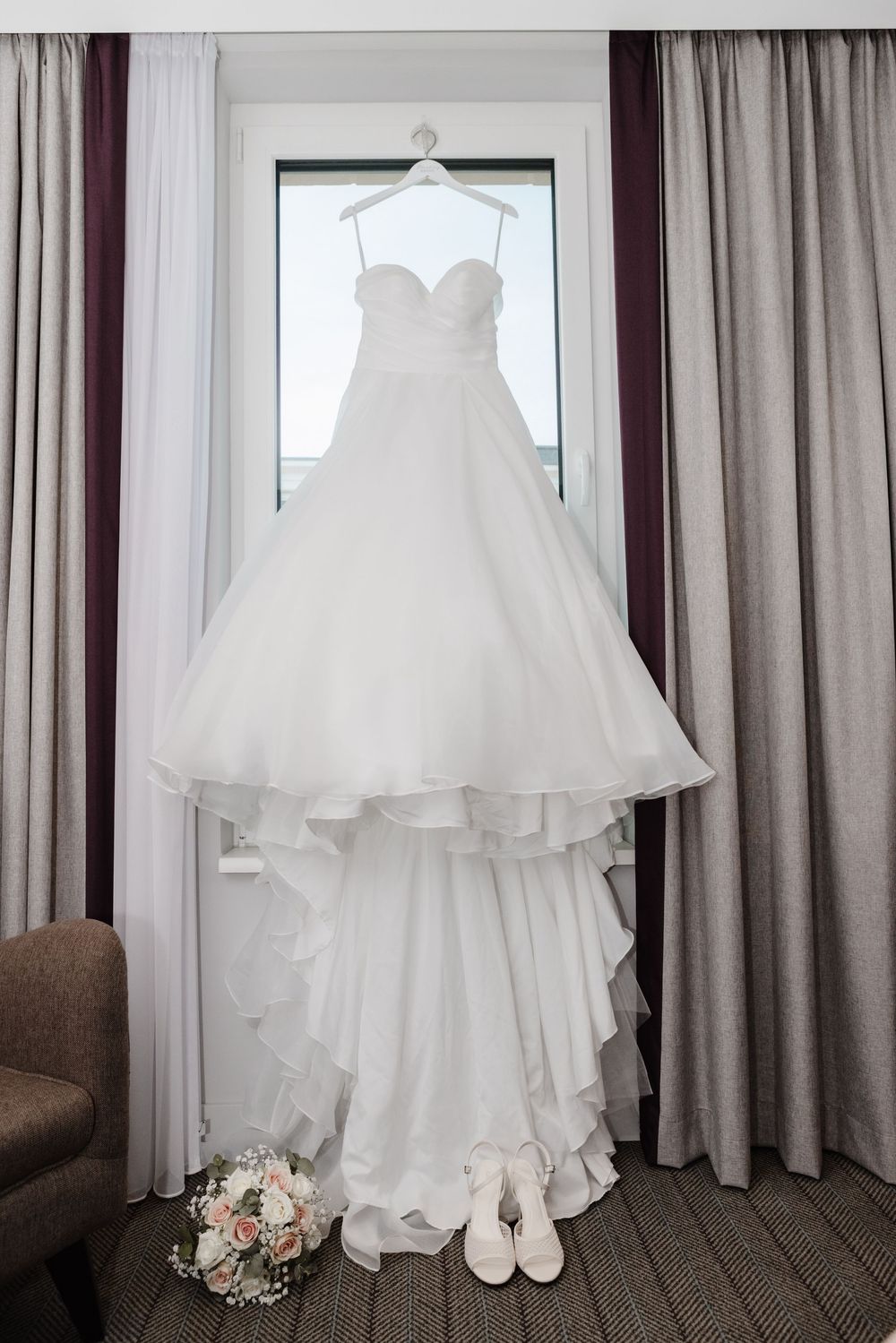 Weißes Brautkleid hängt am Fenster, darunter Brautstrauß und Brautschuhe – Getting-ready zur Trauung in Duisburg-Mitte.