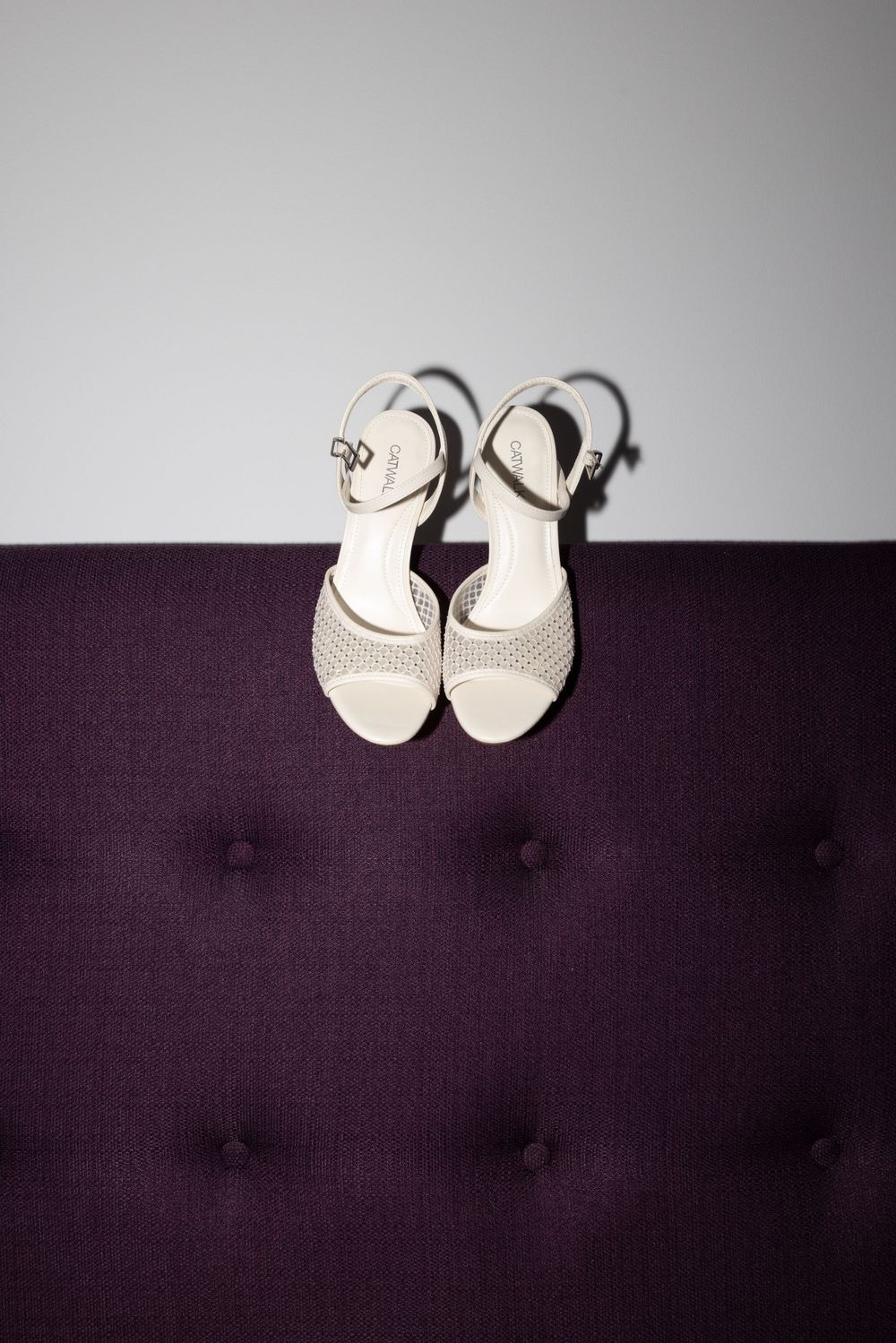 Weiße Brautschuhe mit Riemchen von oben auf auberginefarbenem Sofa – Detailfoto zur standesamtlichen Trauung in Duisburg.