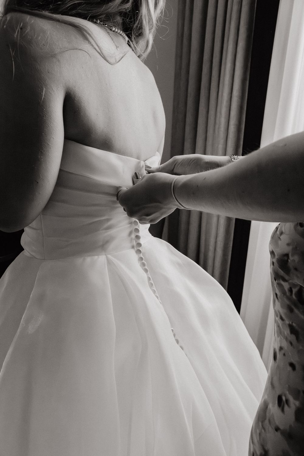Brautkleid wird am Rücken zugeknöpft beim Ankleiden der Braut, Schwarz-Weiß – Getting-ready zur Hochzeit in Duisburg-Mitte.