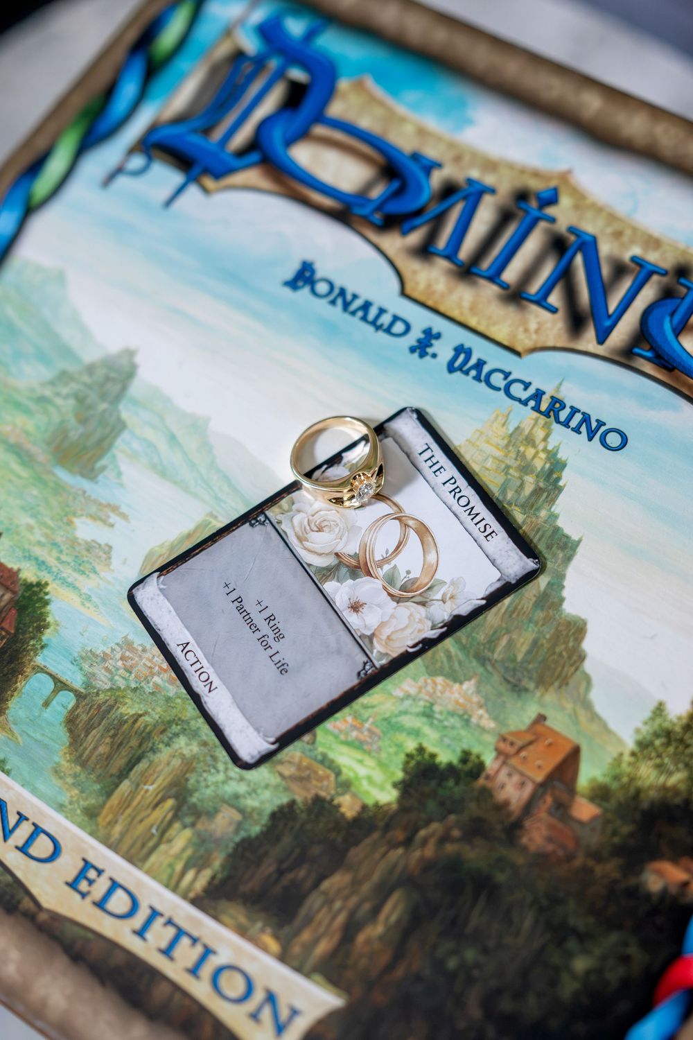 Engagement rings displayed on a Dominion board game card with floral accents, symbolizing a board game proposal.