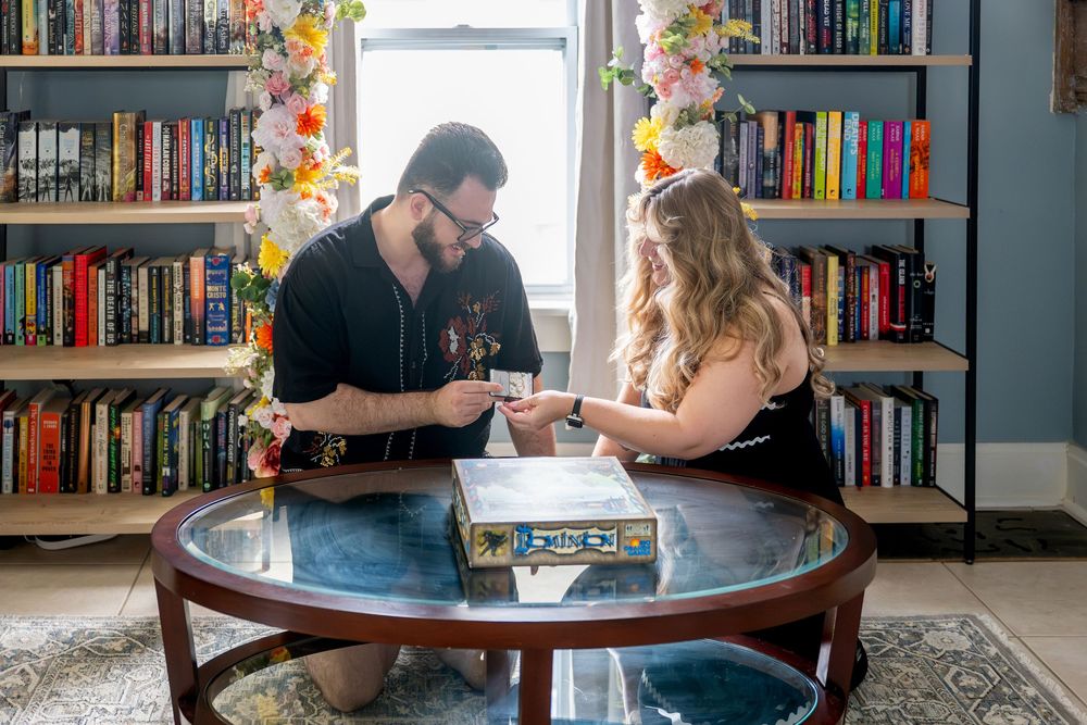 Couple playing a board game together at a glass coffee table surrounded by colorful bookshelves.