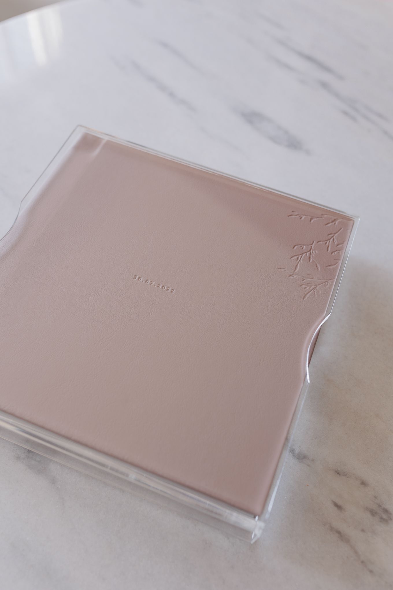 Pink square compact makeup case in clear packaging on a marble surface with floral embossed design.