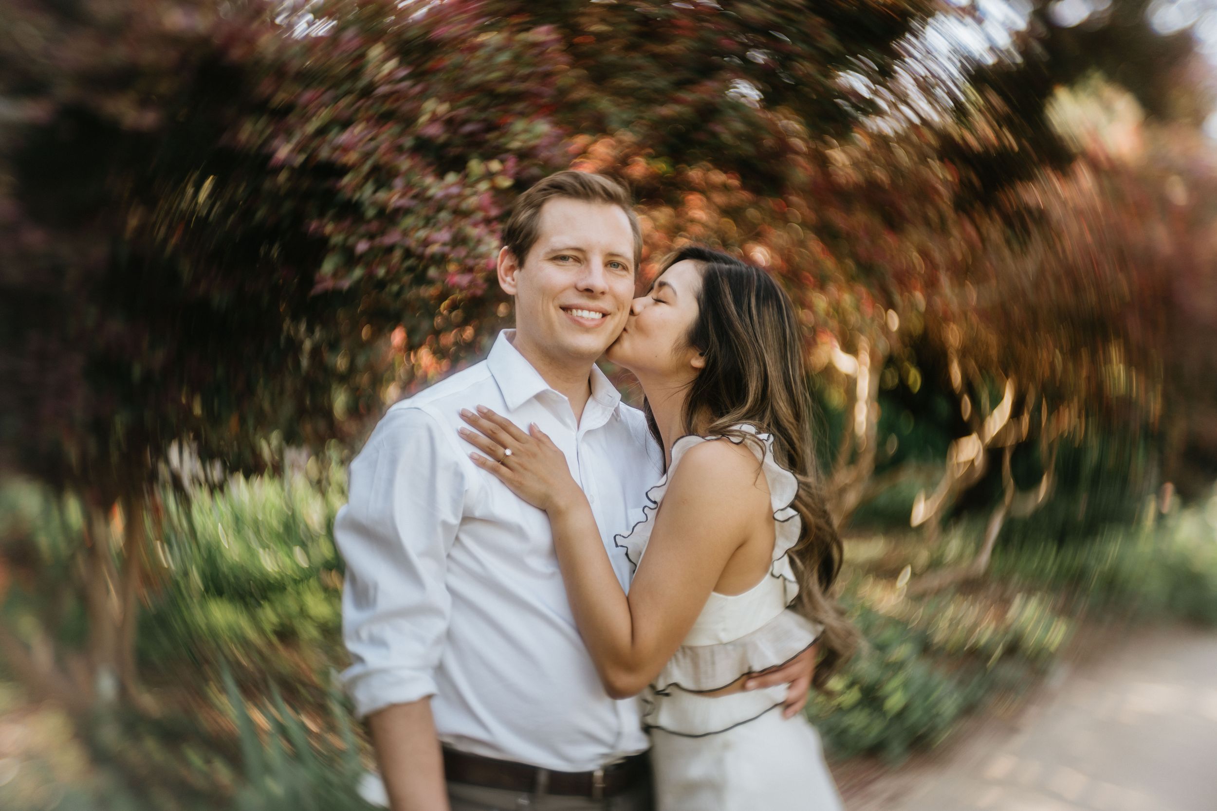 Mariel kissing Jeff beneath blooming trees at the Los Angeles County Arboretum.