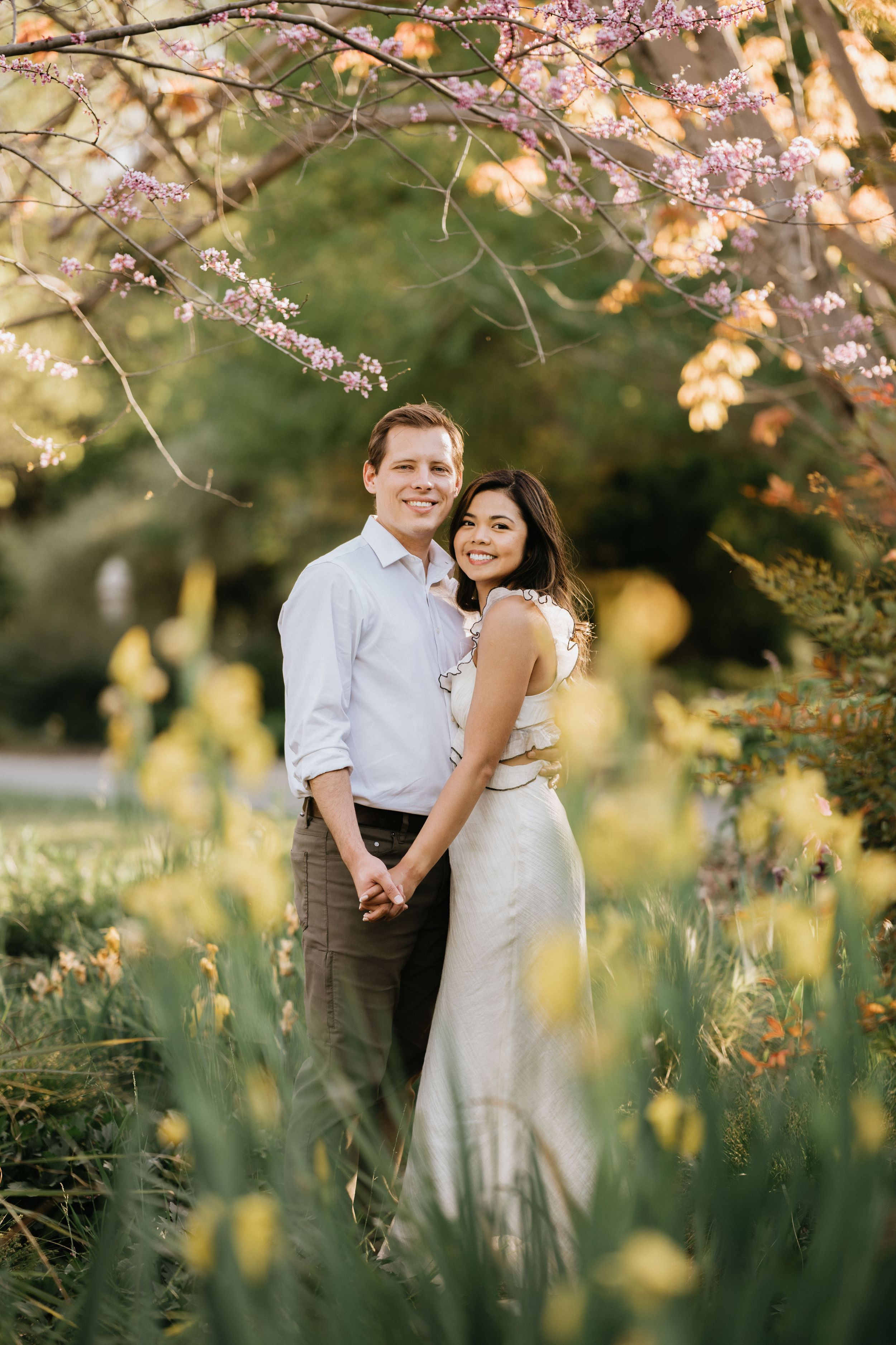 Mariel and Jeff standing beneath blooming cherry blossoms during their engagement session.