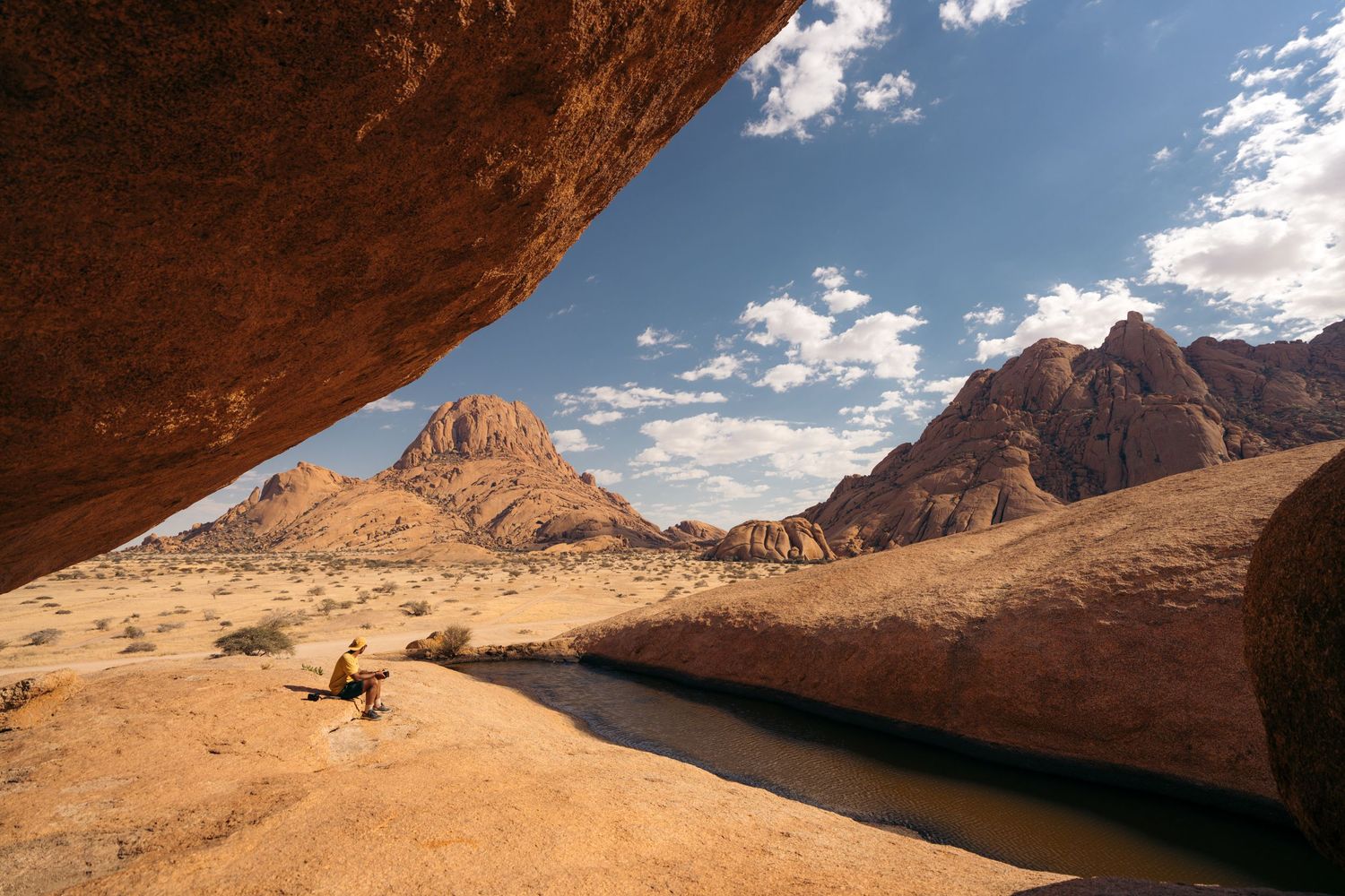 rock pool, homme assis devant une baignoire naturelle d'eau à spitzkoppe avec les montagnes oranges en arrière-plan