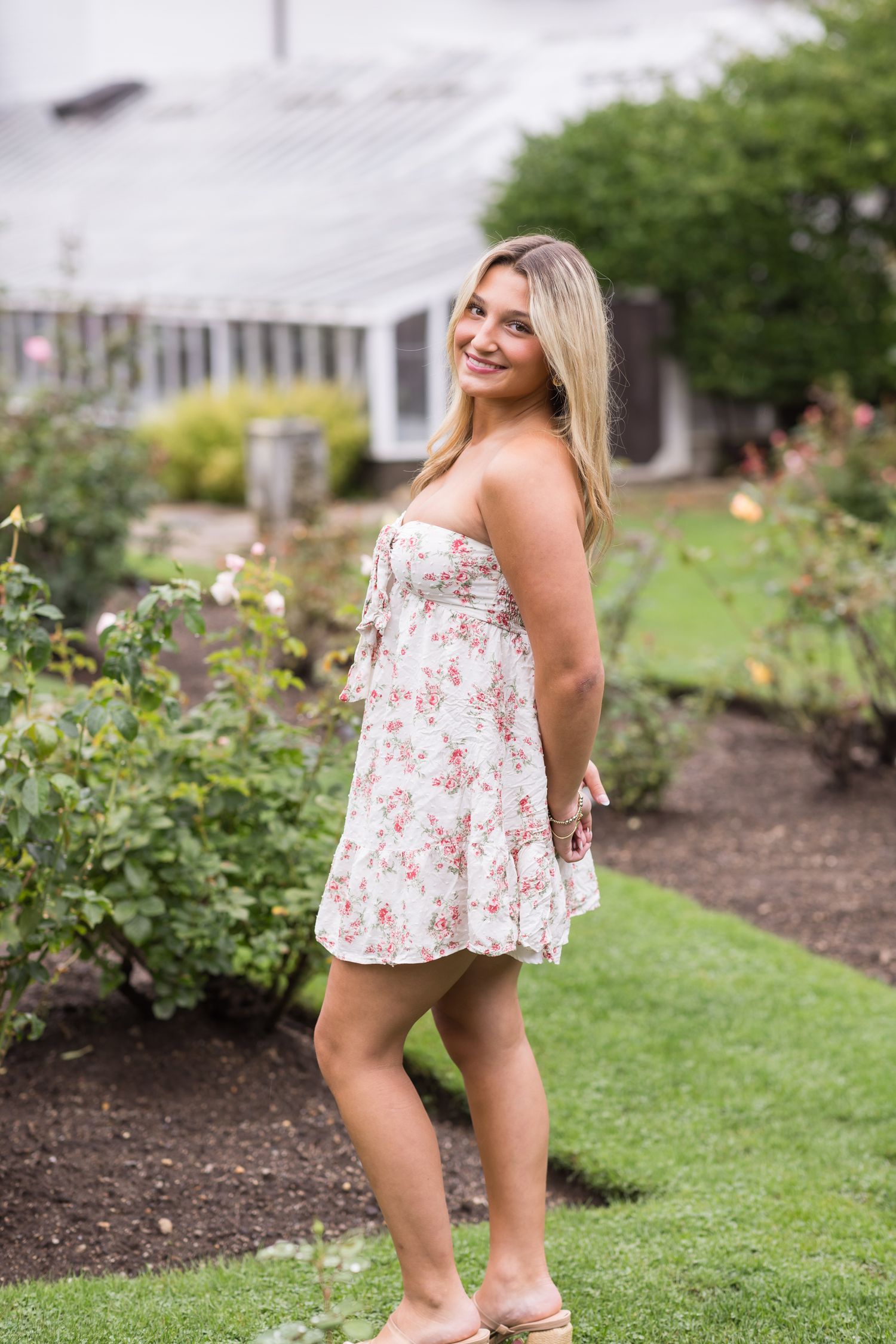 Teen girl wears short floral dress at Fuller Gardens for senior portraits in Hampton, New Hampshire. Hampton York senior photographer