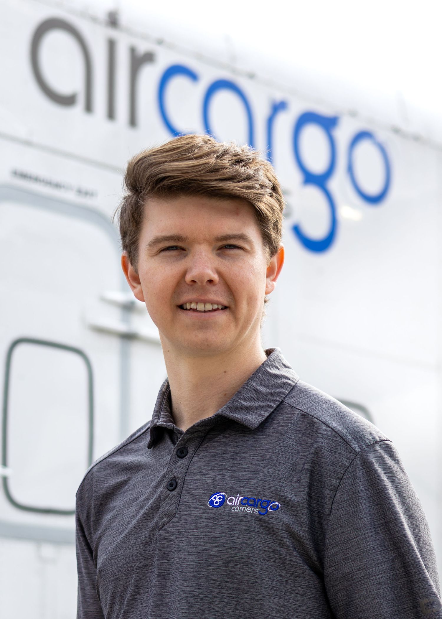 Young man in air cargo company polo shirt standing in front of a cargo aircraft.