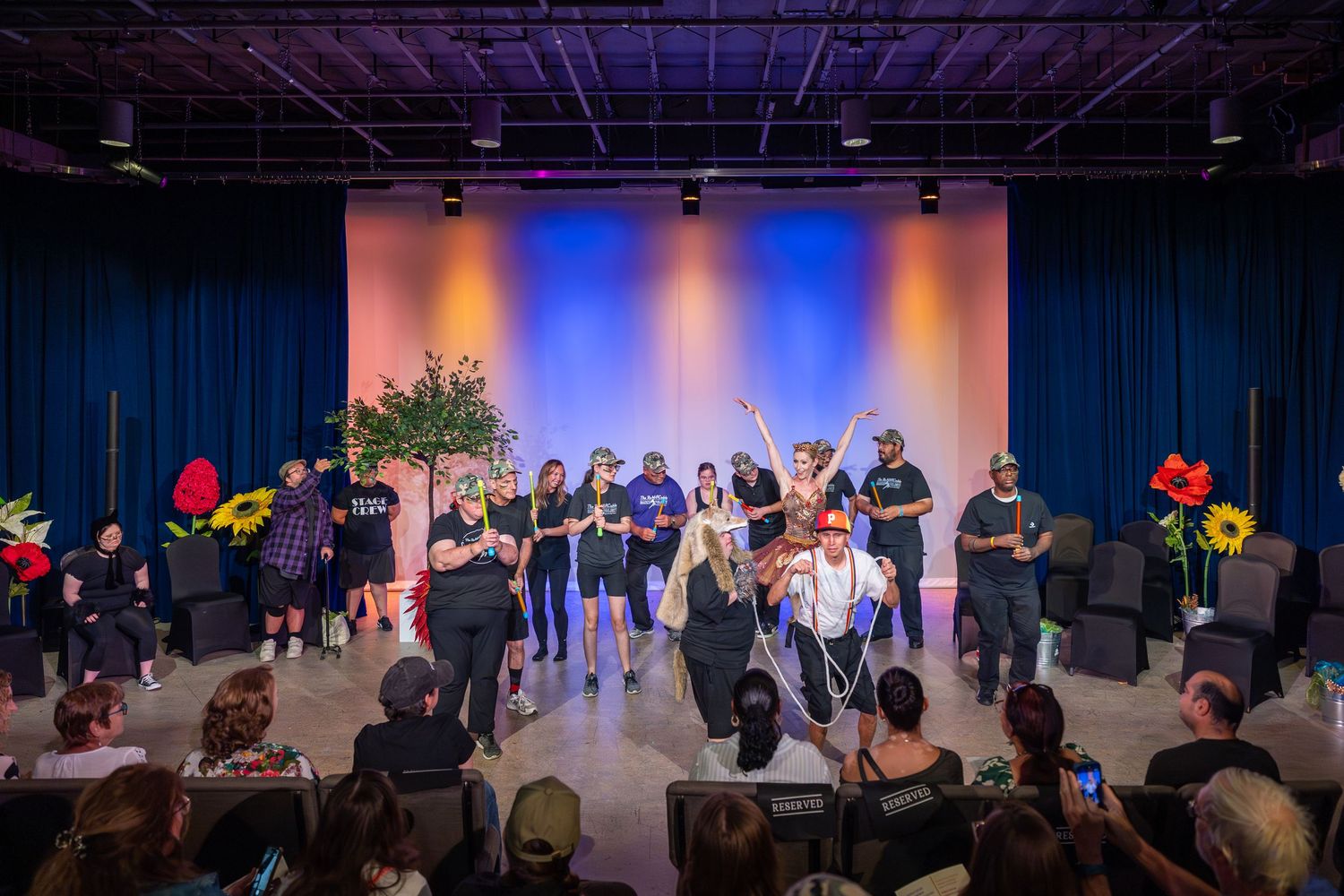 Group of performers on a colorful stage during a live theater production with an audience watching in the foreground.