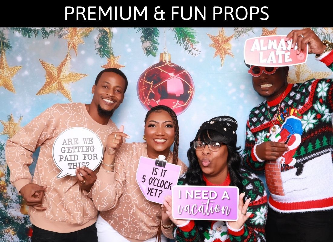 Four friends pose with fun holiday photo booth props including humorous signs at a festive Christmas party backdrop.