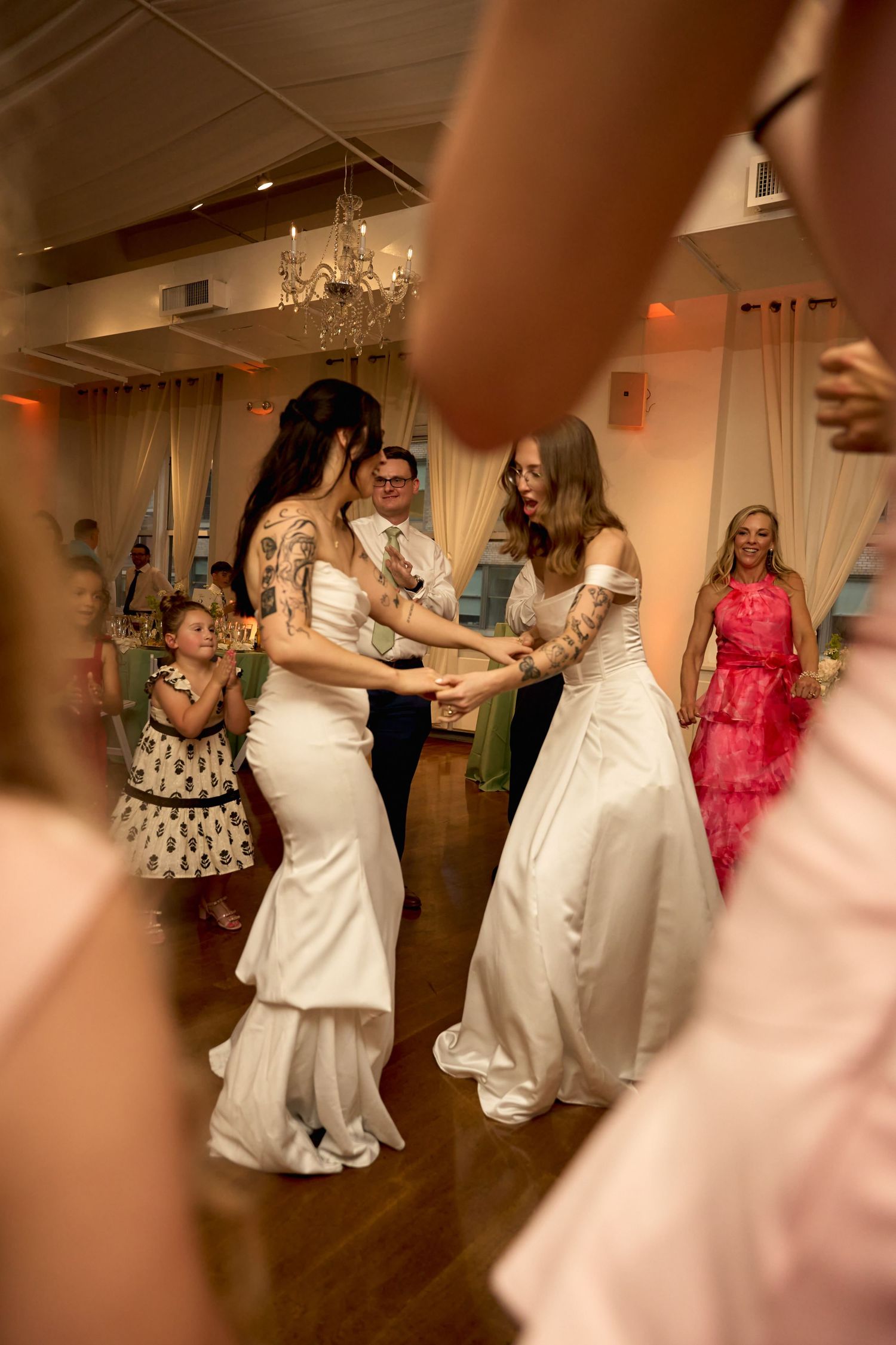 Two brides in white gowns dance together at their wedding reception surrounded by guests.