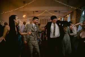 Guests dancing joyfully at a wedding reception with fairy lights decorating the venue ceiling.