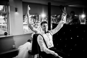 Black and white photo of a bride and groom celebrating at their wedding reception, both raising hands joyfully.