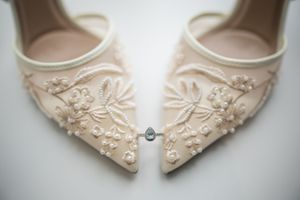 Elegant blush bridal heels with floral embroidery and pearl details displayed with a diamond engagement ring.