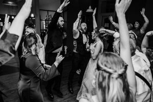 Black and white wedding reception dance floor with bride, groom, and guests celebrating with hands raised.