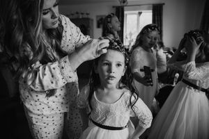 Black and white photo of a woman placing a floral crown on a young flower girl in a white dress before a wedding.