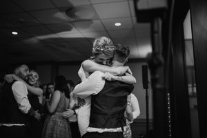 Black and white photo of couple sharing emotional embrace on wedding dance floor surrounded by guests.