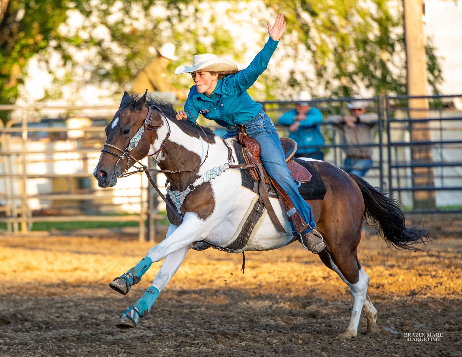 Cowgirl in teal shirt rides a brown and white horse during a barrel racing rodeo competition outdoors.